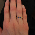 Hand wearing a 14K gold ring with small sapphire stones on a dark background