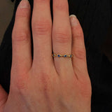 Hand wearing a 14K gold ring with small sapphire stones on a dark background