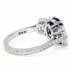A platinum ring featuring a deep blue sapphire and clear diamonds,  set on a diamond and filigree band against a white background.