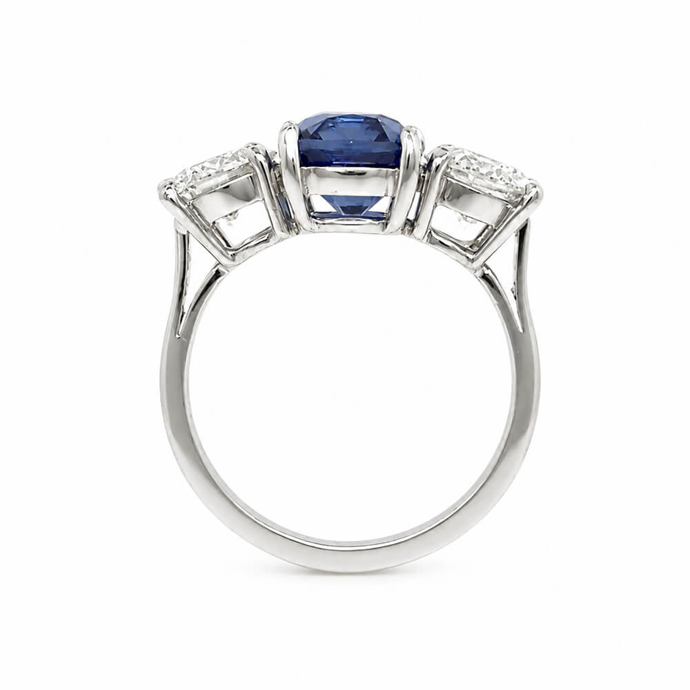 A platinum ring featuring a central rectangular blue sapphire gemstone flanked by two smaller round diamonds, shown on a plain white background.