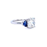 A platinum ring featuring a large clear diamond accented by a half moon blue sapphire son the side, set against a plain white background.
