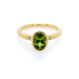 An 18kt yellow gold ring with a green peridot centerpiece, presented against a white background.