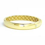 A polished 18k yellow gold bangle bracelet with an engraved pattern on the inside.