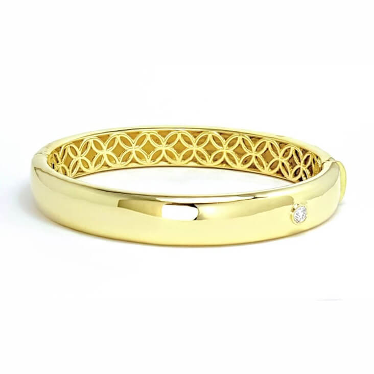 A polished 18k yellow gold bangle bracelet with an engraved pattern on the inside.