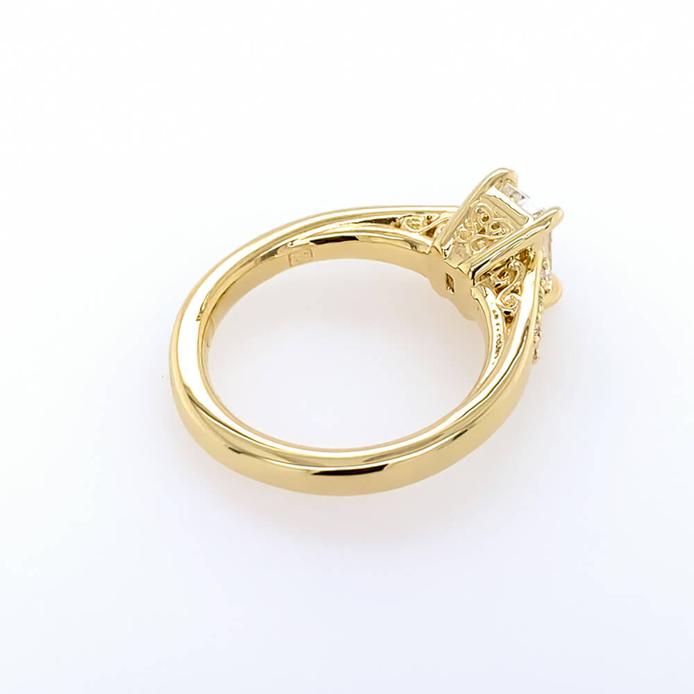 An 18K yellow gold ring with a polished band and an openwork filigree-style crown setting, photographed on a clean white background.