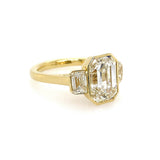 An 18K yellow gold ring featuring a large emerald-cut diamond center stone and two smaller emerald-cut diamonds on either side, set against a plain white background.