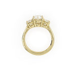 An 18K yellow gold three-stone ring with an oval-cut center stone and smaller side stones, shown on a plain white background.