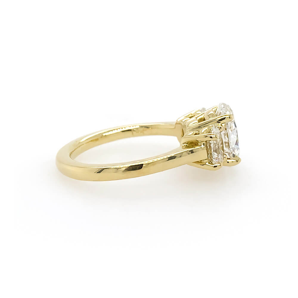 An 18K yellow gold ring featuring a three oval clear diamonds in prong settings, shown from a side angle on a plain white background.