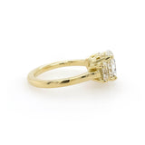 An 18K yellow gold ring featuring a three oval clear diamonds in prong settings, shown from a side angle on a plain white background.