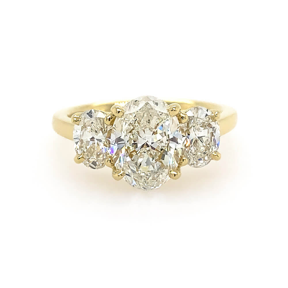 An 18K yellow gold three-stone ring featuring a large oval center diamond flanked by two smaller oval side diamonds, set against a plain white background.