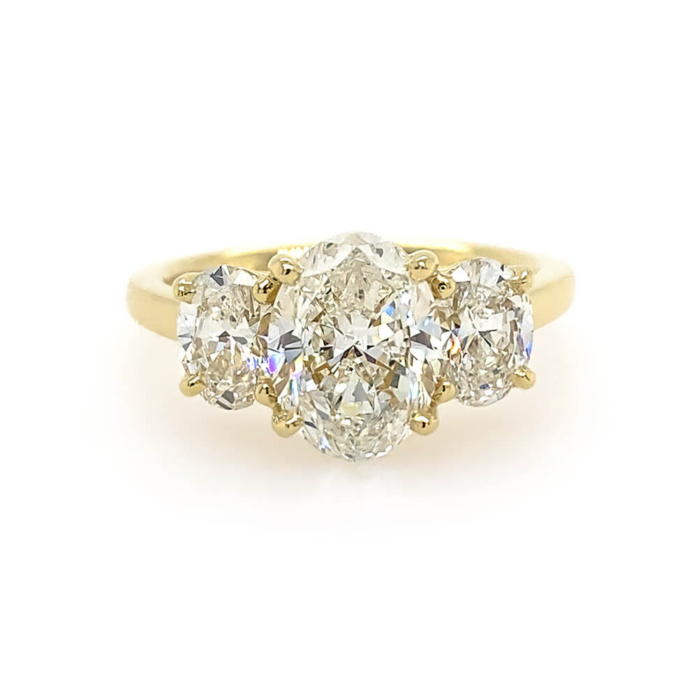 An 18K yellow gold three-stone ring featuring a large oval center diamond flanked by two smaller oval side diamonds, set against a plain white background.