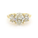 An 18K yellow gold three-stone ring featuring a large oval center diamond flanked by two smaller oval side diamonds, set against a plain white background.