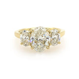 An 18K yellow gold three-stone ring featuring a large oval center diamond flanked by two smaller oval side diamonds, set against a plain white background.