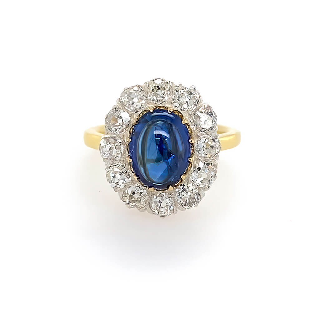 A vintage-style ring featuring an oval-cut blue sapphire surrounded by a halo of clear diamonds on an 18K yellow gold band, set against a plain white background.