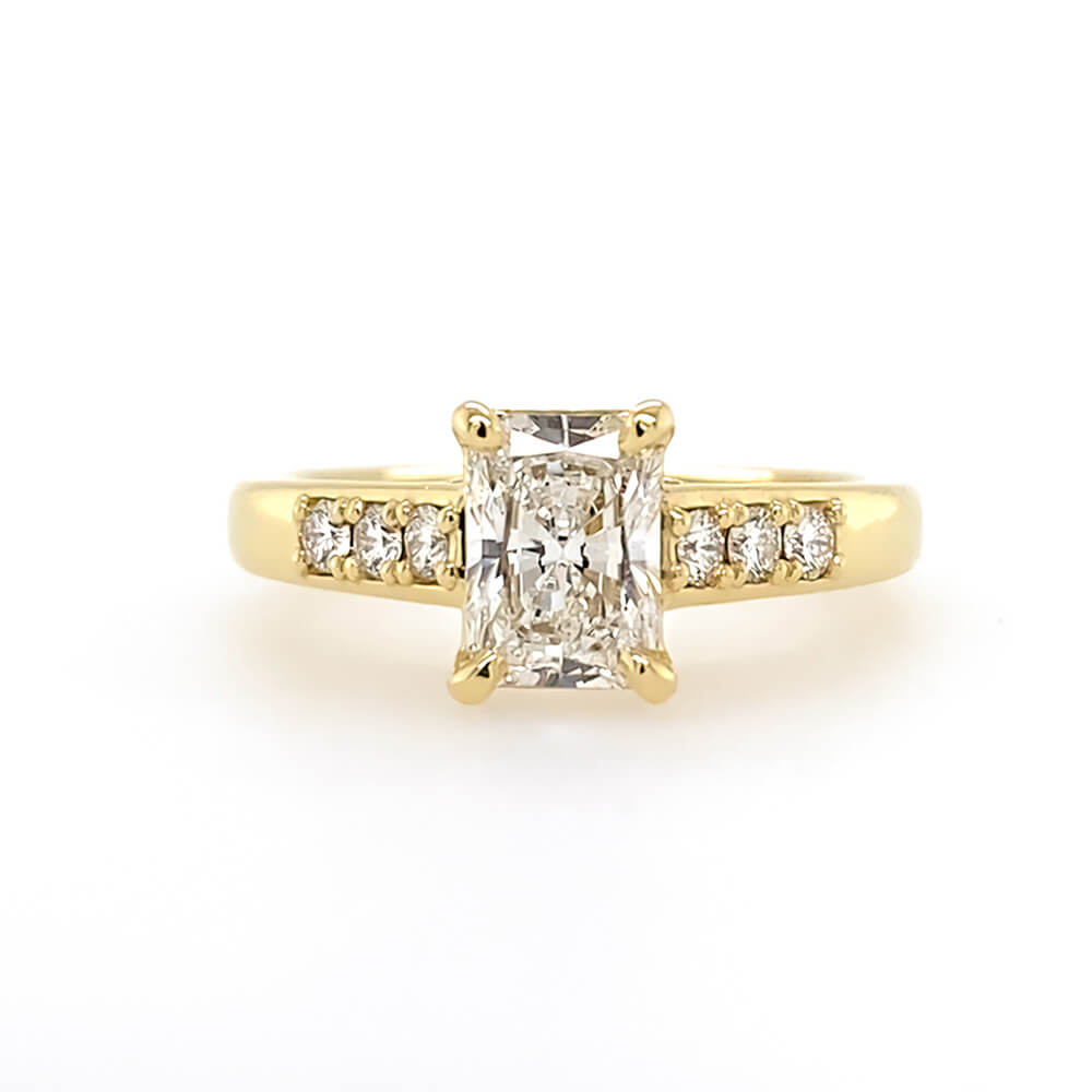 An 18K yellow gold engagement ring featuring a large rectangular radiant-cut center diamond flanked by smaller round diamonds on the band, set against a plain white background.