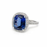 A cushion-cut blue sapphire ring with a diamond halo and a platinum pavé diamond band, set against a plain white background.