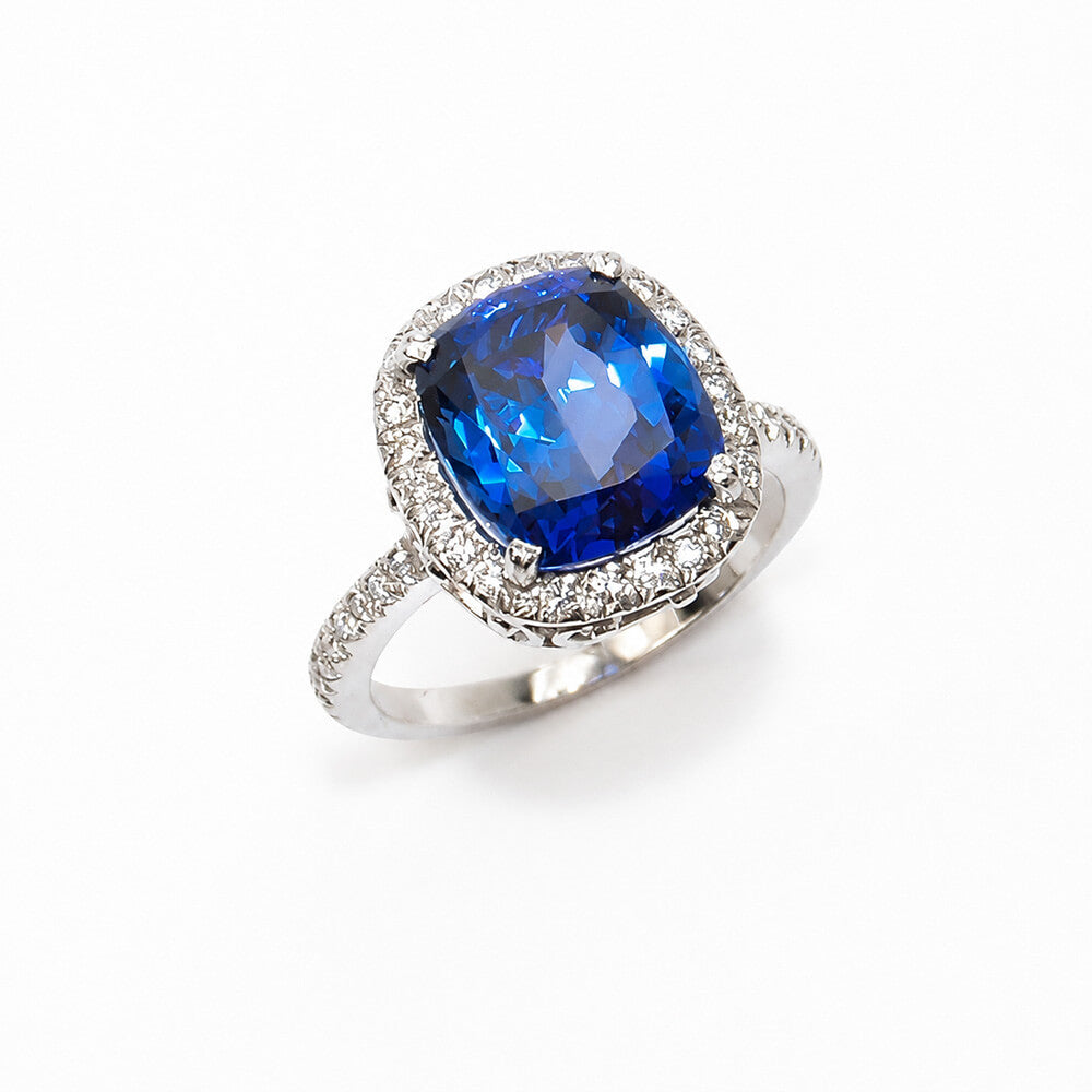 A cushion-cut blue sapphire ring with a halo of small clear diamonds and a platinum band, photographed on a clean white background.