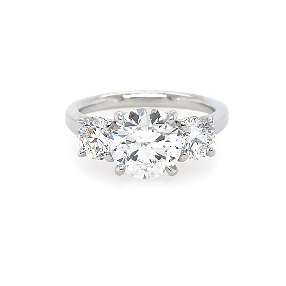A three-stone diamond ring with a brilliant round center diamond flanked by two smaller round diamonds on a polished platinum band, set against a plain white background.