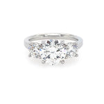 A three-stone diamond ring with a brilliant round center diamond flanked by two smaller round diamonds on a polished platinum band, set against a plain white background.