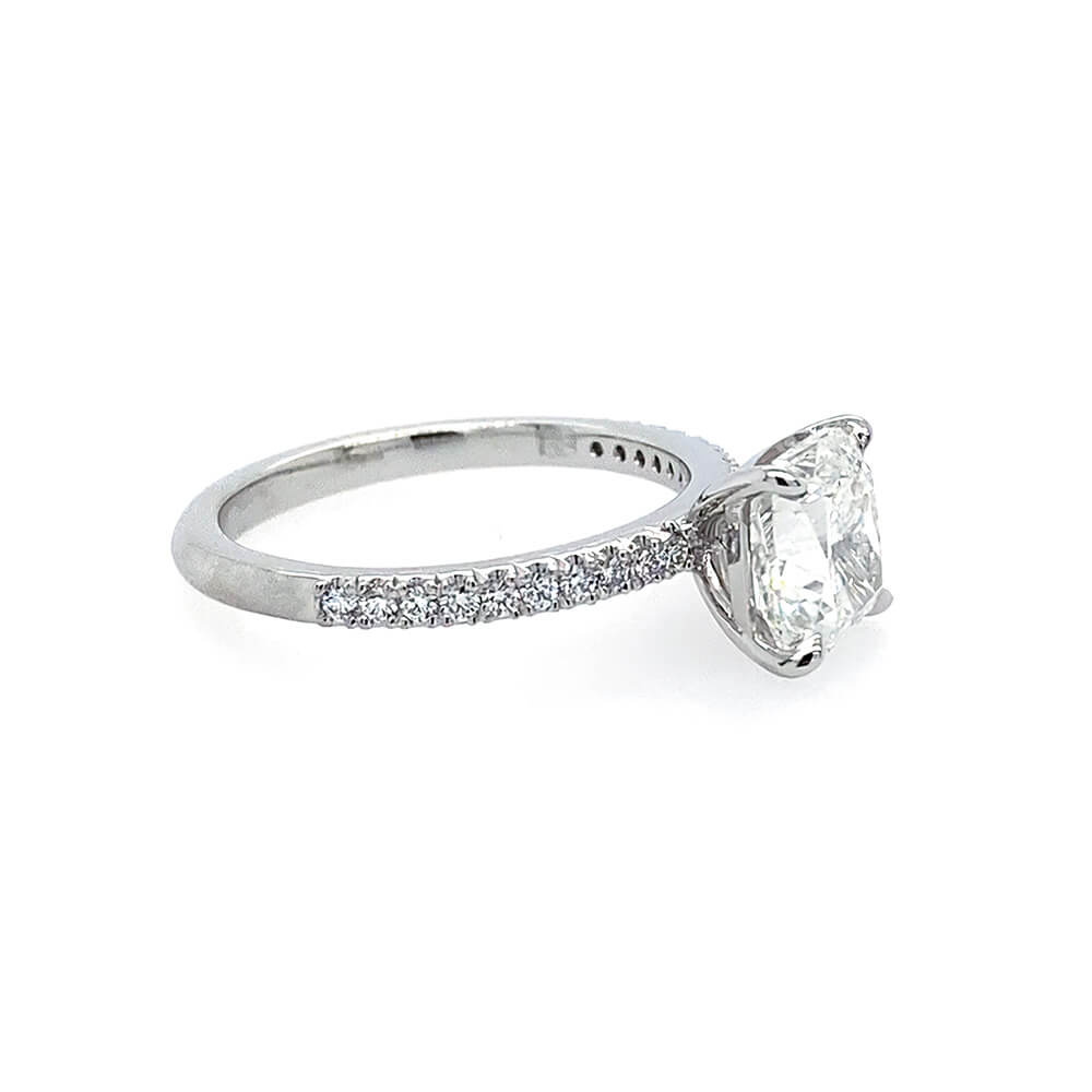 A platinum diamond engagement ring featuring a large cushion-cut center stone in a four-prong setting, with a pavé band of small round diamonds on a white background.