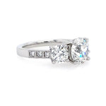 A platinum three-stone diamond engagement ring with a round center diamond and round side diamonds, set on a white background.