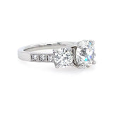 A platinum three-stone diamond engagement ring with a round center diamond and round side diamonds, set on a white background.