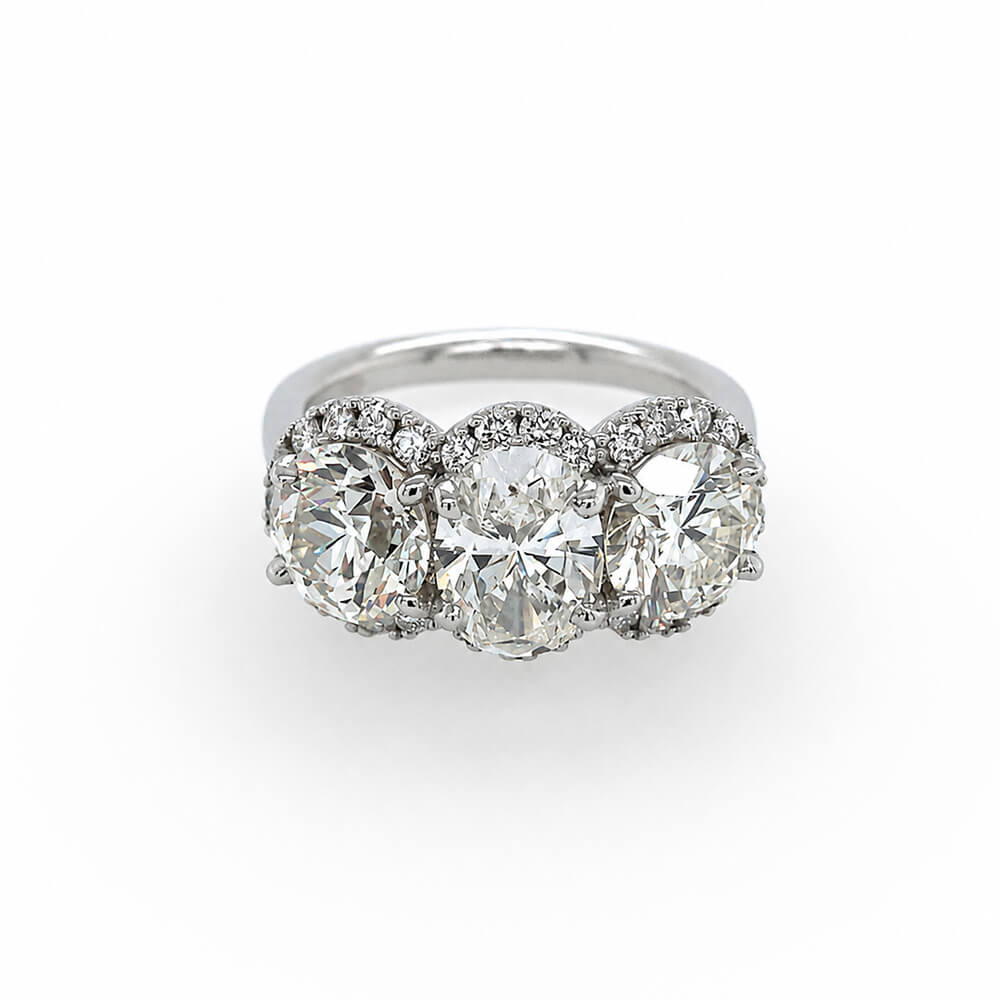 A three-stone diamond ring featuring three large round-cut diamonds surrounded by smaller diamond halos, set on a polished platinum band against a plain white background.