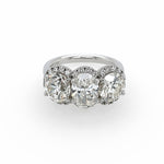 A three-stone diamond ring featuring three large round-cut diamonds surrounded by smaller diamond halos, set on a polished platinum band against a plain white background.