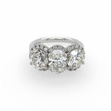 A three-stone diamond ring featuring three large round-cut diamonds surrounded by smaller diamond halos, set on a polished platinum band against a plain white background.