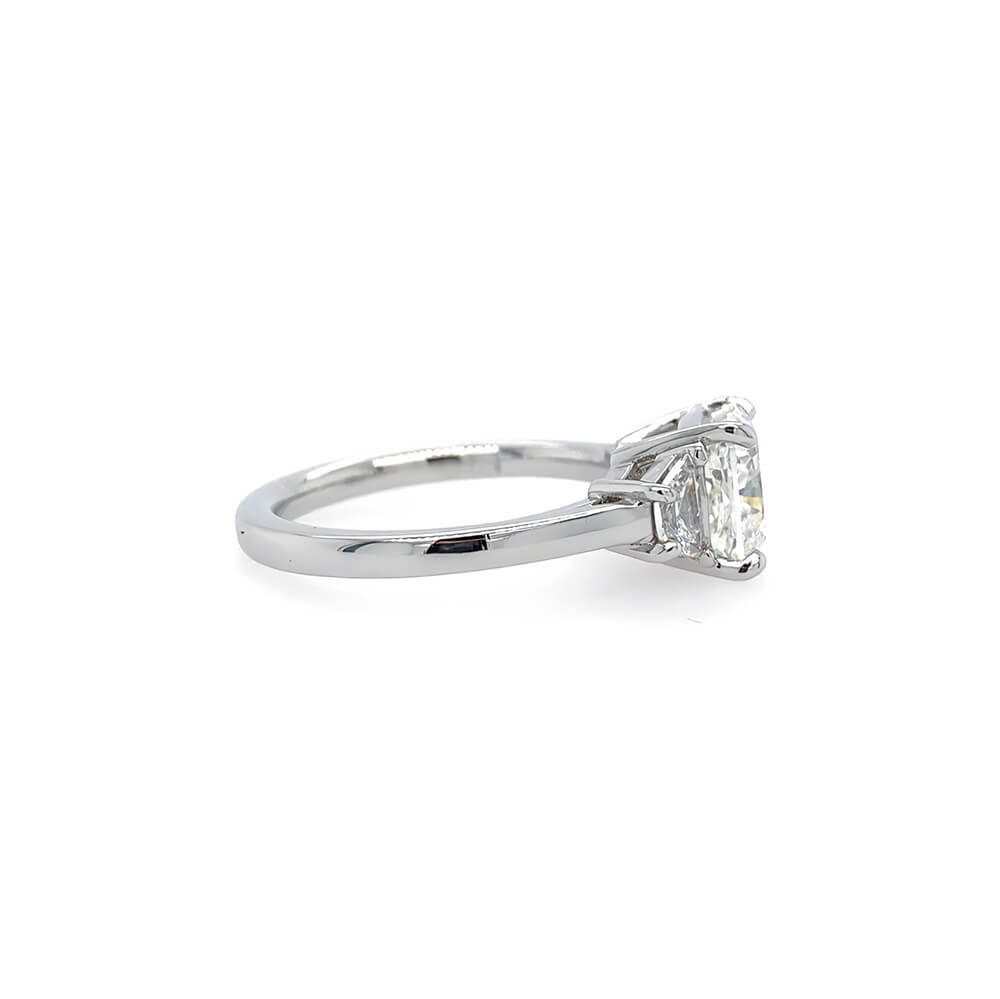 A platinum ring featuring a rectangular clear center diamond and two smaller side diamonds, shown from a side view on a plain white background.