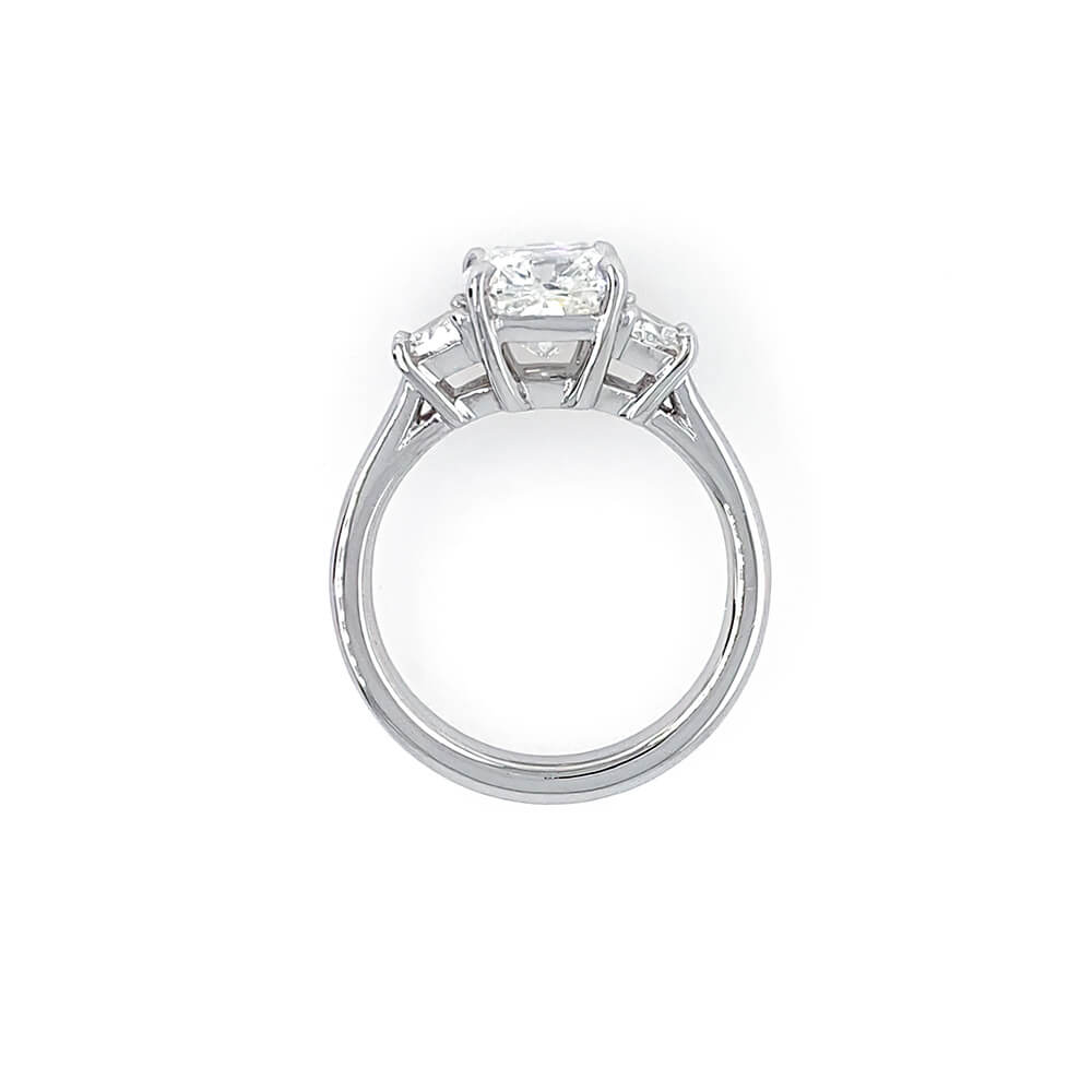 A platinum ring featuring a rectangular clear center diamond and two smaller side diamonds, shown from a side view on a plain white background.