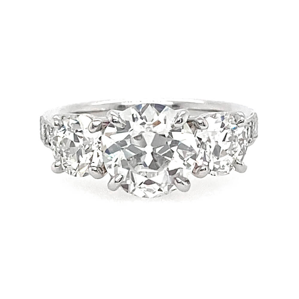 A three-stone diamond ring featuring a round center diamond flanked by two round side diamonds on a polished platinum band, set against a plain white background.