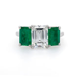 A platinum ring featuring a central Diamond with surrounding emeralds set in a classic prong setting.