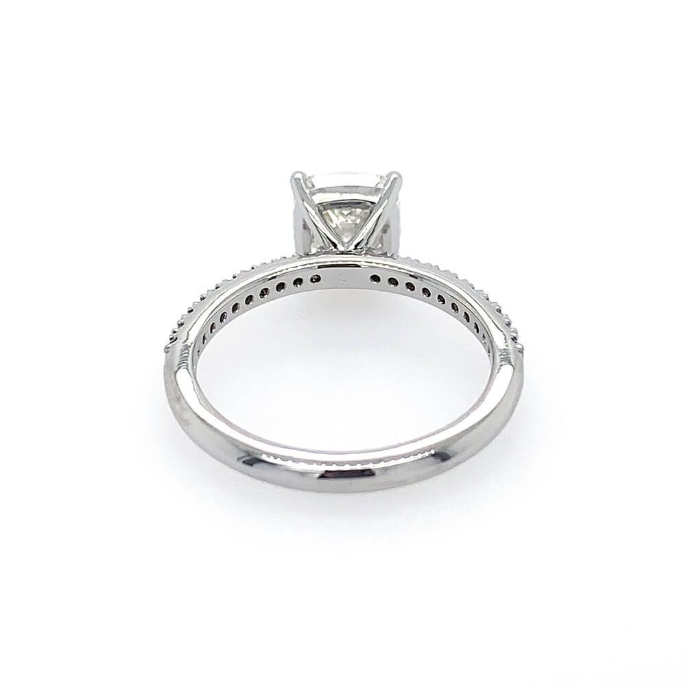A platinum diamond ring shown from the underside, featuring a cushion-cut center stone in a four-prong setting and a pavé band with small accent diamonds, photographed on a white background.