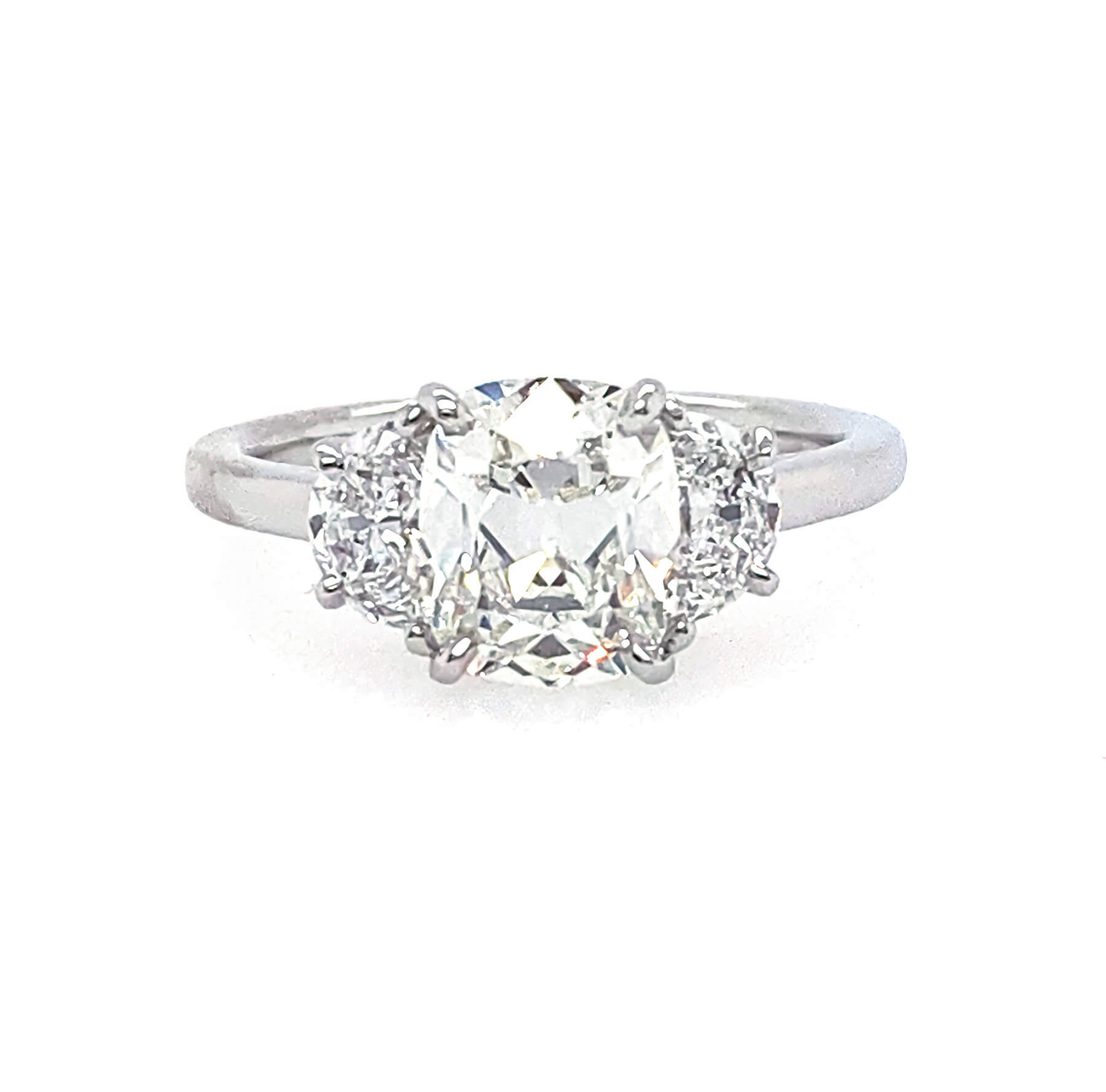 A three-stone diamond engagement ring featuring a central old-mine-cut diamond flanked by two half-moon diamonds on a polished platinum band, set against a plain white background.