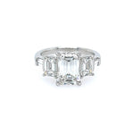 A custom platinum ring featuring a large emerald-cut center stone with two smaller matching emerald-cut side stones, and tapered baguettes, set against a plain white background.