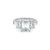 A custom platinum ring featuring a large emerald-cut center stone with two smaller matching emerald-cut side stones, and tapered baguettes, set against a plain white background.