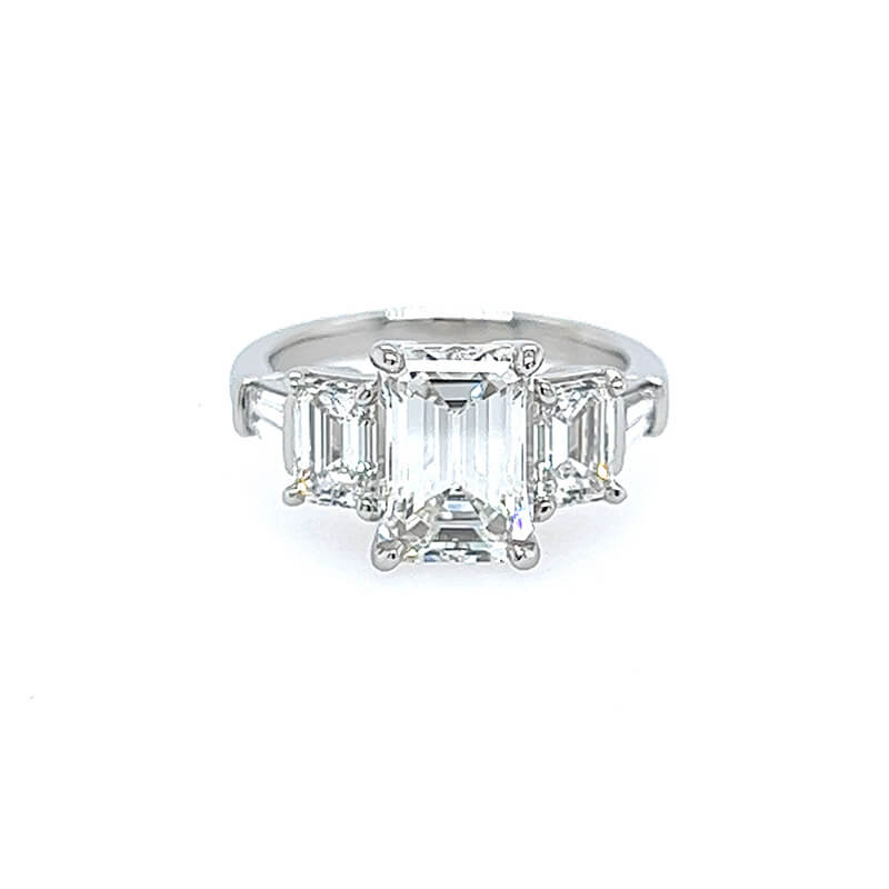 A custom platinum ring featuring a large emerald-cut center stone with two smaller matching emerald-cut side stones, and tapered baguettes, set against a plain white background.
