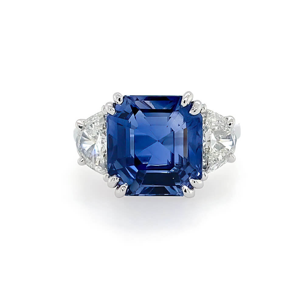 A square cushion-cut sapphire ring with diamond side stones in a platinum setting, photographed on a clean white background.