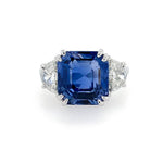A square cushion-cut sapphire ring with diamond side stones in a platinum setting, photographed on a clean white background.