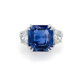 A square cushion-cut sapphire ring with diamond side stones in a platinum setting, photographed on a clean white background.