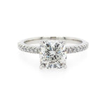A square cushion cut diamond engagement ring with a platinum band set with small pavé diamonds, shown on a plain white background.