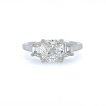A three-stone diamond ring featuring a central cushion-cut diamond flanked by two half-moon-cut diamonds on a polished platinum band, set against a plain white background.