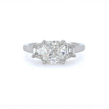 A three-stone diamond ring featuring a central cushion-cut diamond flanked by two half-moon-cut diamonds on a polished platinum band, set against a plain white background.
