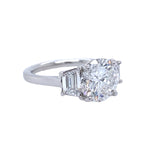 A custom-designed platinum round diamond ring with a trapezoid side stone, displayed against a white background.