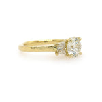 A custom designed round brilliant diamond ring with trapezoid side diamonds in hammered 18K yellow gold