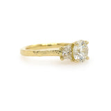 A custom designed round brilliant diamond ring with trapezoid side diamonds in hammered 18K yellow gold