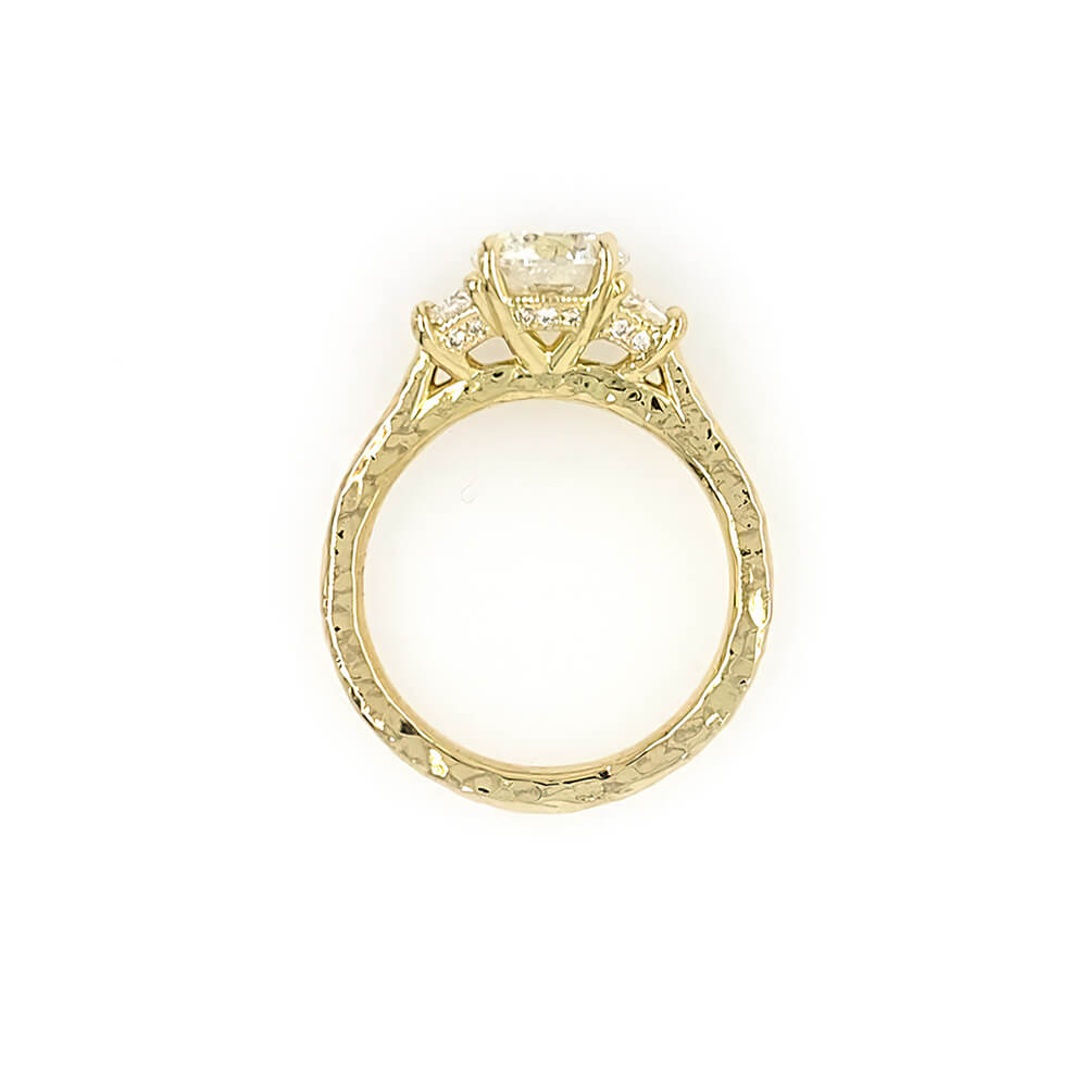 A custom designed round brilliant diamond ring with trapezoid side diamonds in hammered 18K yellow gold