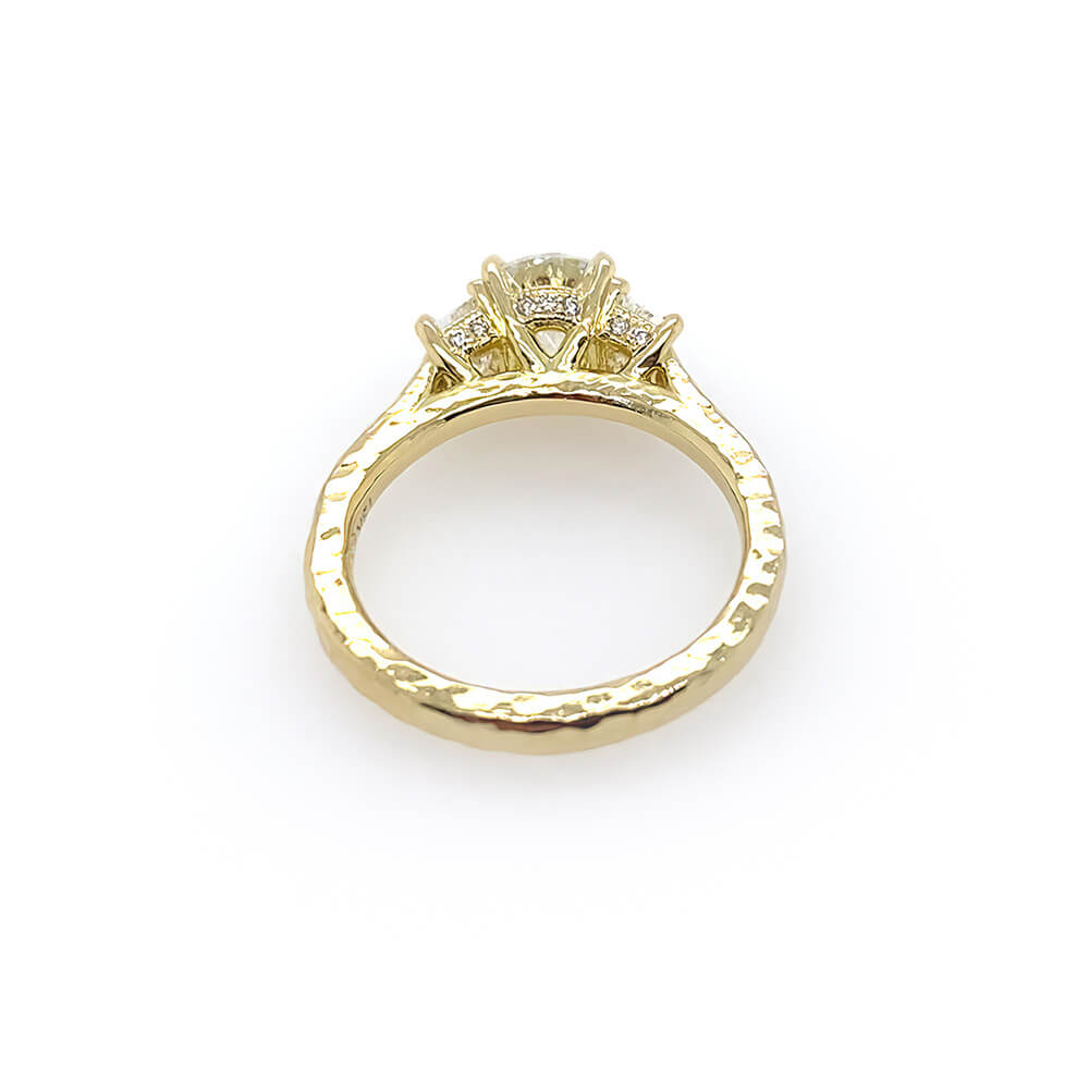 A custom designed round brilliant diamond ring with trapezoid side diamonds in hammered 18K yellow gold