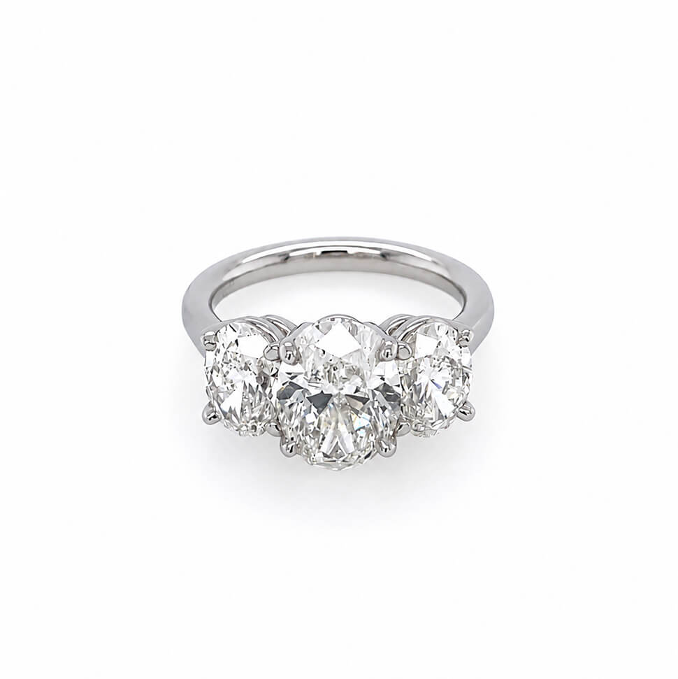 A custom designed three-stone diamond ring featuring a large oval center diamond flanked by two oval side diamonds, set in a polished platinum band against a plain white background.